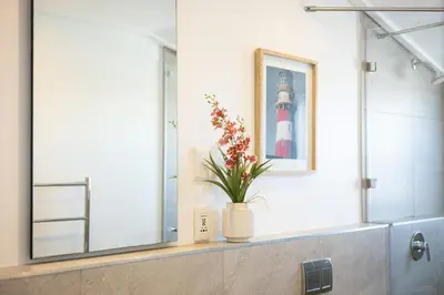 a bathroom with a lighthouse picture and a vase with flowers at Mountain-View Studio - Hermanus Waterfront Apartments in Hermanus