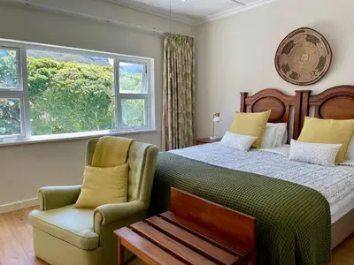a bedroom with a bed and a chair and a window at Wholeness Accommodation in Hermanus
