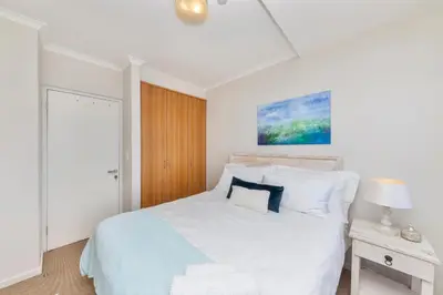 a white bedroom with a bed and a night stand at Horizon Bay 206 by HMH in Cape Town