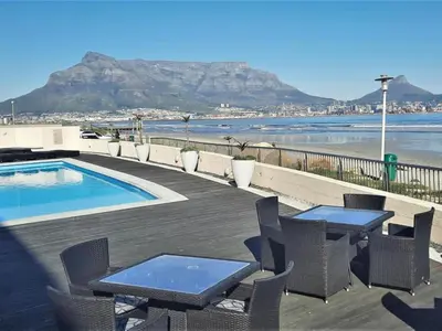 a patio with tables and chairs next to a swimming pool at Lagoon Shoreline 2 Bedroom Apartment in Cape Town