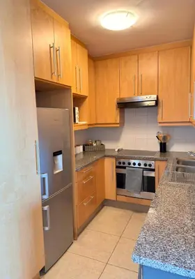 a kitchen with wooden cabinets and a stainless steel refrigerator at Beautiful 2 Bedroom Apartment with Ocean Views, Bloubergstrand in Cape Town