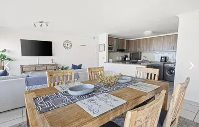 a kitchen and living room with a wooden table and chairs at The Continental Sea Spray in Cape Town