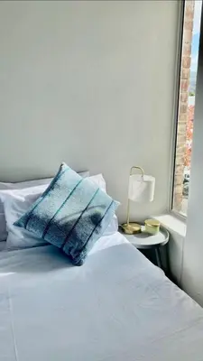 a bed with a blue pillow on it next to a window at The Madge Self Catering in Paarl
