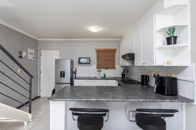 a kitchen with white cabinets and a counter with stools at Century on Lake B31 by CTHA in Cape Town