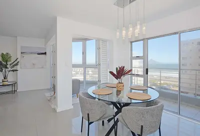 a dining room with a glass table and chairs at Ocean View B401 by CTHA in Bloubergstrand