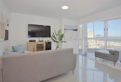 a white living room with a couch and a television at Ocean View B401 by CTHA in Bloubergstrand
