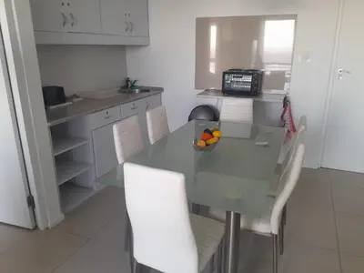 a kitchen with a glass table and white chairs at Sunset 786 Holiday Accommodation-Room 208 in Strand
