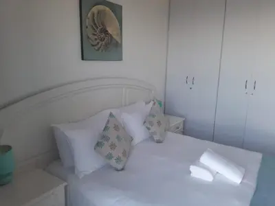 a white bed with pillows and a picture on the wall at Sunset 786 Holiday Accommodation-Room 208 in Strand