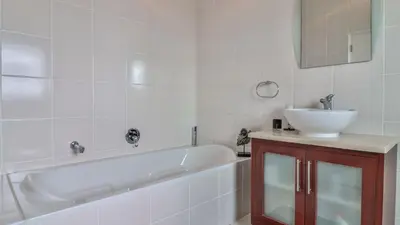 a bathroom with a tub and a sink and a mirror at C-Onrus in Hermanus