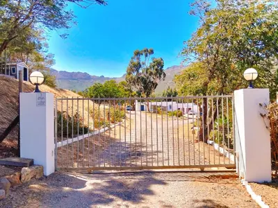 a gate to a driveway with mountains in the background at Into the Sunset Manor in Gordonʼs Bay
