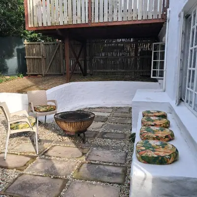 a patio with a fire pit and a chair and a deck at Vermont Garden Cottage in Hermanus