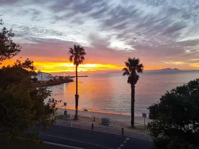 two palm trees on a beach with a sunset at 'Top Flat' Apartment with Easy Beach Access, Sea front sleeps 5 in Gordonʼs Bay