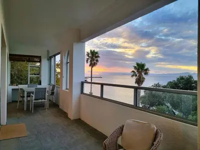 a room with a balcony with a view of the ocean at 'Top Flat' Apartment with Easy Beach Access, Sea front sleeps 5 in Gordonʼs Bay