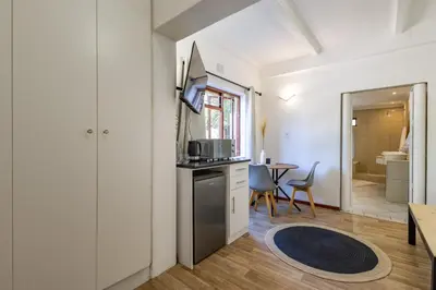a room with a kitchen and a table with chairs at Bed On Boucher in Durbanville