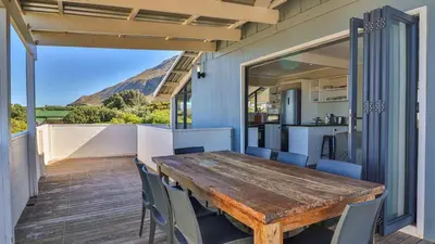 a wooden table and chairs on a balcony with a kitchen at BluCabana 500m from Main Beach in Bettyʼs Bay