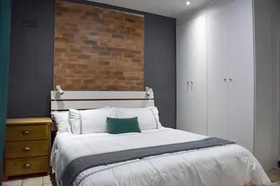 a bedroom with a bed and a brick wall at Blade Flatlet in Silver Sands