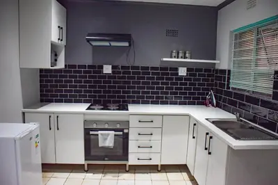 a small kitchen with white cabinets and black tiles at Blade Flatlet in Silver Sands