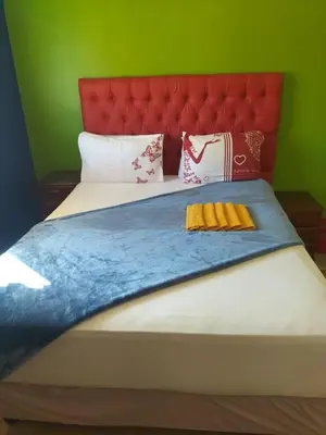 a large bed with a red headboard and some pillows at Neo & Ruks Guest house parow 1 in Avondale