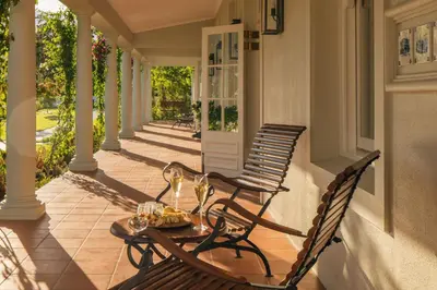 a porch with two chairs and a table with wine glasses at Leeu Estates in Franschhoek