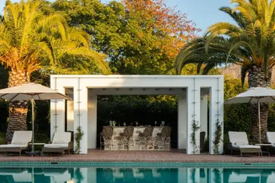 a pavilion by a pool with chairs and umbrellas at Leeu House in Franschhoek