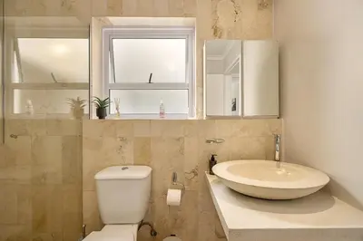 a bathroom with a toilet and a sink and two windows at The Island Beach House in Cape Town