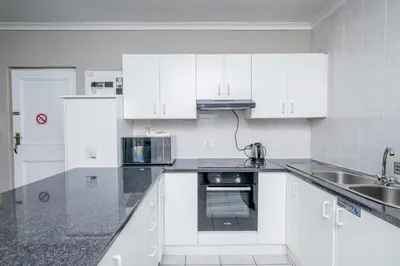 a white kitchen with white cabinets and a sink at Prime Executive Apartments 2 in Durbanville