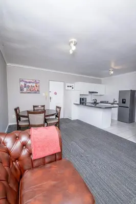 a living room with a brown leather couch and a kitchen at Prime Executive Apartments 2 in Durbanville