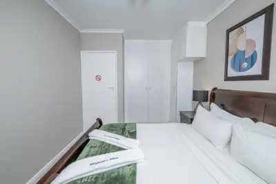 a white bedroom with a bed with two towels on it at Prime Executive Apartments 2 in Durbanville