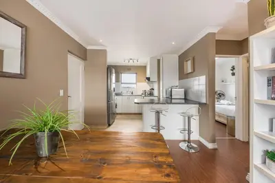 a living room with a kitchen with a wooden floor at Modern City Apartment with Balcony & Braai in Cape Town