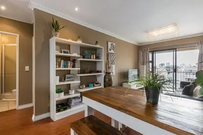 a living room with a wooden table and bookshelves at Modern City Apartment with Balcony & Braai in Cape Town