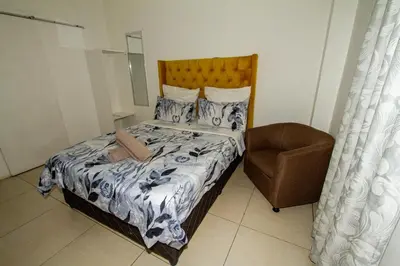 a small bedroom with a bed and a chair at Lodge Luxe, Cozy Bedrooms, Free WiFi, Robust Security in Cape Town
