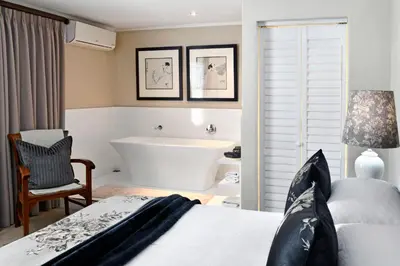 a bedroom with a tub and a bed and a bath room at Le Petit Bijou Aparthotel in Franschhoek