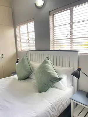 a white bed with two green pillows on it at Nunu's Self Catering Apartment in Paarl
