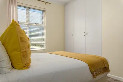 a white bedroom with a yellow pillow on a bed at Elegant Apartment with Pool and Balcony Views in Cape Town