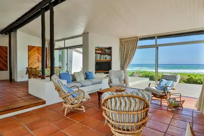 a living room with a couch and chairs and the ocean at Turtle Drum ON THE BEACH in Bettyʼs Bay
