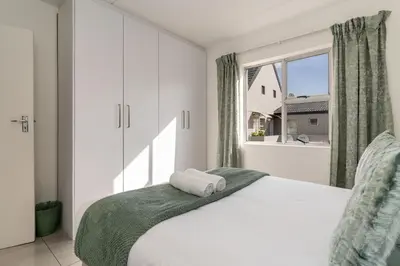 a white bedroom with a bed with a window at Manhattan Square 17 in Cape Town