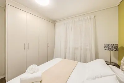 a white bedroom with a bed and a window at The Lagoon Beachfront Apartment in Cape Town