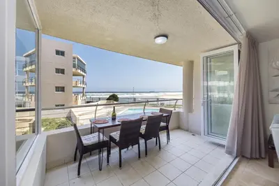 a balcony with a table and chairs and a view of the ocean at The Lagoon Beachfront Apartment in Cape Town