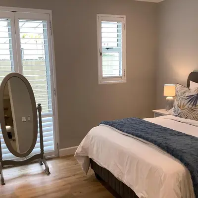 a bedroom with a bed with a mirror and two windows at Apartment Franschhoek 121 Lermitage in Franschhoek