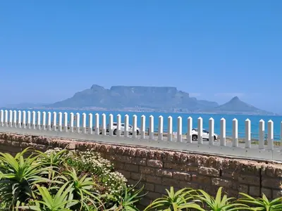 a white fence on a road next to the ocean at Aandvari Zeezicht in Cape Town