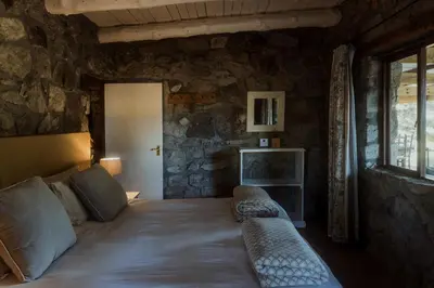 a bedroom with a bed in a stone wall at Glen Oakes Farm Stay in Hartebeest Rivier