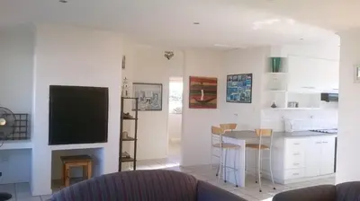 a living room with a kitchen with a table and a tv at Aandvari Sunset Court in Cape Town