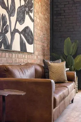 a brown leather couch in a room with a brick wall at My Venue at Avemore in Onder-Papegaaiberg