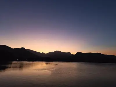 a sunset over a lake with mountains in the background at La Jolie Dauphine Guest House in Franschhoek
