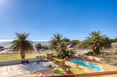 a view of a swimming pool and palm trees at Ocean & Mountain View Escape, 100m Walk to beach - Gordon's Bay in Gordonʼs Bay