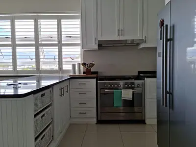 a kitchen with white cabinets and a stainless steel refrigerator at Penthouse on the beach, Jacuzzi with 3 bedrooms in Cape Town