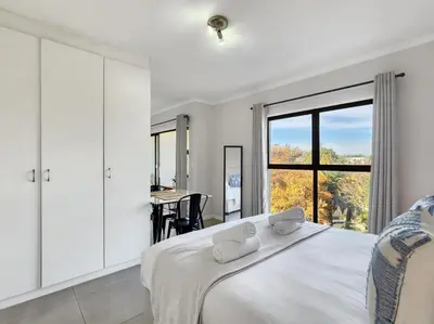 a white bedroom with a large bed and a window at Rivers Edge Apartment in Rondebosch with Balcony in Cape Town