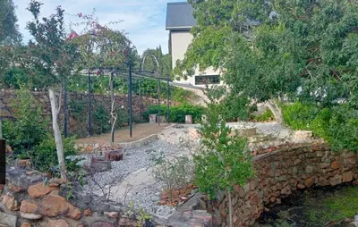 a garden with a stone retaining wall and trees at Studio at Providence in Hermanus