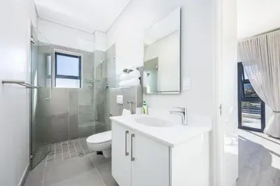 a white bathroom with a toilet and a sink at Esplanade Hermanus Central Sea Views in Hermanus