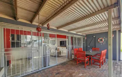 a dining room with a table and red chairs at Sealax Cottage Fleurpark in Gordonʼs Bay